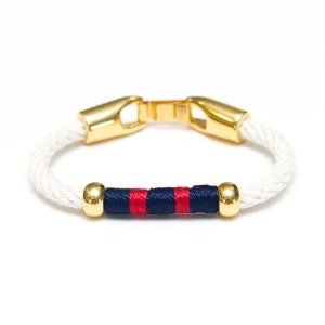May include: A white rope bracelet with a gold clasp and a red and navy blue striped band.