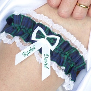 May include: A white lace garter with a blue and green plaid fabric band. The garter has two white satin ribbons with the names "Rachel" and "David" written in green.