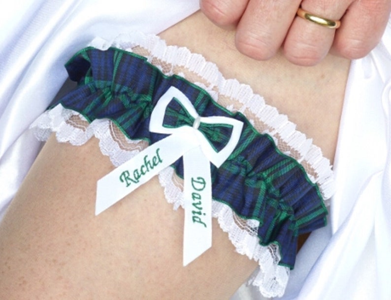 May include: A white lace garter with a blue and green plaid fabric band. The garter has two white satin ribbons with the names "Rachel" and "David" written in green.