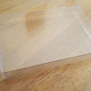 May include: A clear plastic display box with a rectangular shape. The box is empty and has a smooth surface.