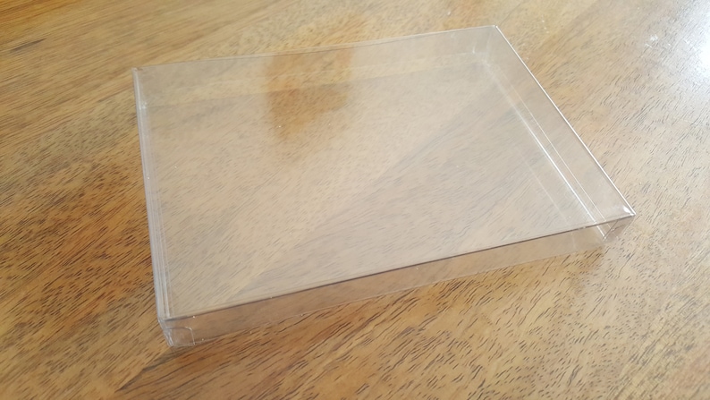 May include: A clear plastic display box with a rectangular shape. The box is empty and has a smooth surface.