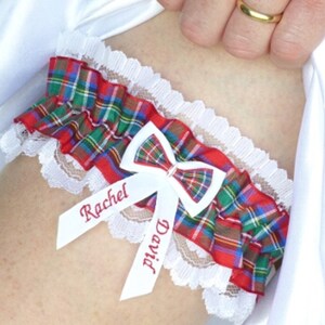 May include: A white lace garter with a red, green, and blue plaid bow and two white satin ribbons with the names "Rachel" and "David" embroidered in red.