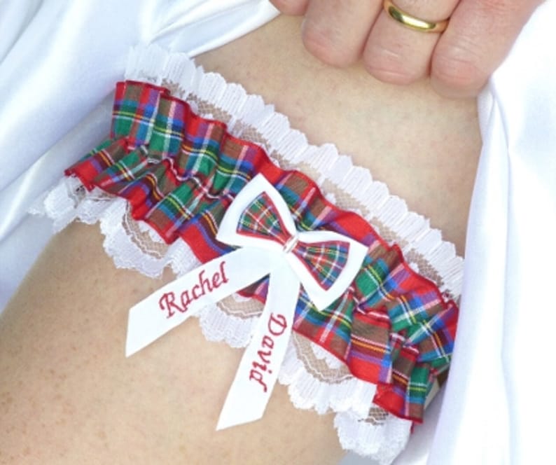 May include: A white lace garter with a red, green, and blue plaid bow and two white satin ribbons with the names "Rachel" and "David" embroidered in red.