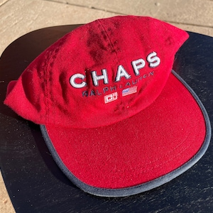 May include: Red baseball cap with a white embroidered logo that says "CHAPS RALPH LAUREN" with a small American flag and a "CH" logo.