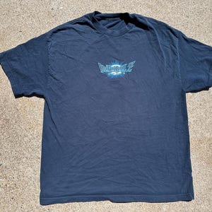 May include: Dark blue t-shirt with the text "Dragon Ball Z" in a stylized, light blue font. The graphic is centered on the chest. The shirt is made of a soft material and has short sleeves.