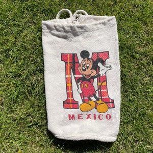 May include: White canvas tote bag with a red and black tartan design and a cartoon image of Mickey Mouse. The bag says "Mexico" at the bottom.