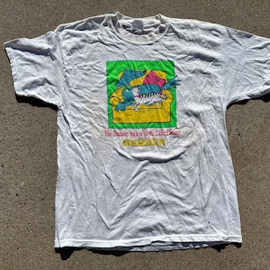 May include: White t-shirt with a green, yellow, pink, and blue graphic of a dog and cat sitting in a chair. The text "The Humane Society of the United States MEMBER" is printed below the graphic.