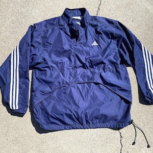 May include: A navy blue windbreaker jacket with white stripes on the sleeves and a small Adidas logo on the chest.