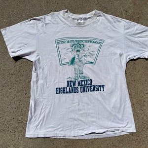 May include: White t-shirt with a green and blue graphic of a cartoon person holding a chalkboard with the text "NTSP Math/Sciences Program" and the text "New Mexico Highlands University".