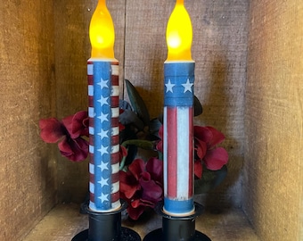 May include: Two battery-operated candles with a red, white and blue American flag design. The candles are in black candle holders.