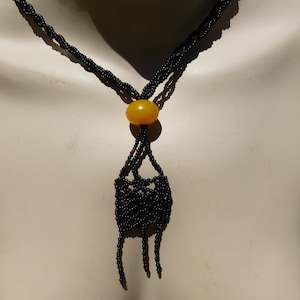 May include: A black beaded necklace with a yellow bead at the center and a tassel at the bottom.