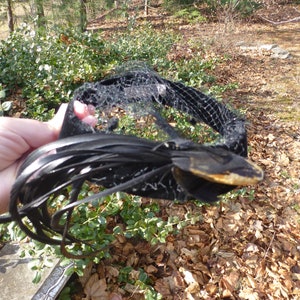 May include: A black vintage hat with a black net veil and a black feather trim. The hat is in good condition and has a unique design.