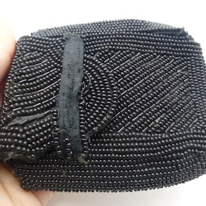 May include: A black beaded purse with a flap closure. The purse is made of small, round beads that are sewn together in a pattern. The flap has a black fabric lining.