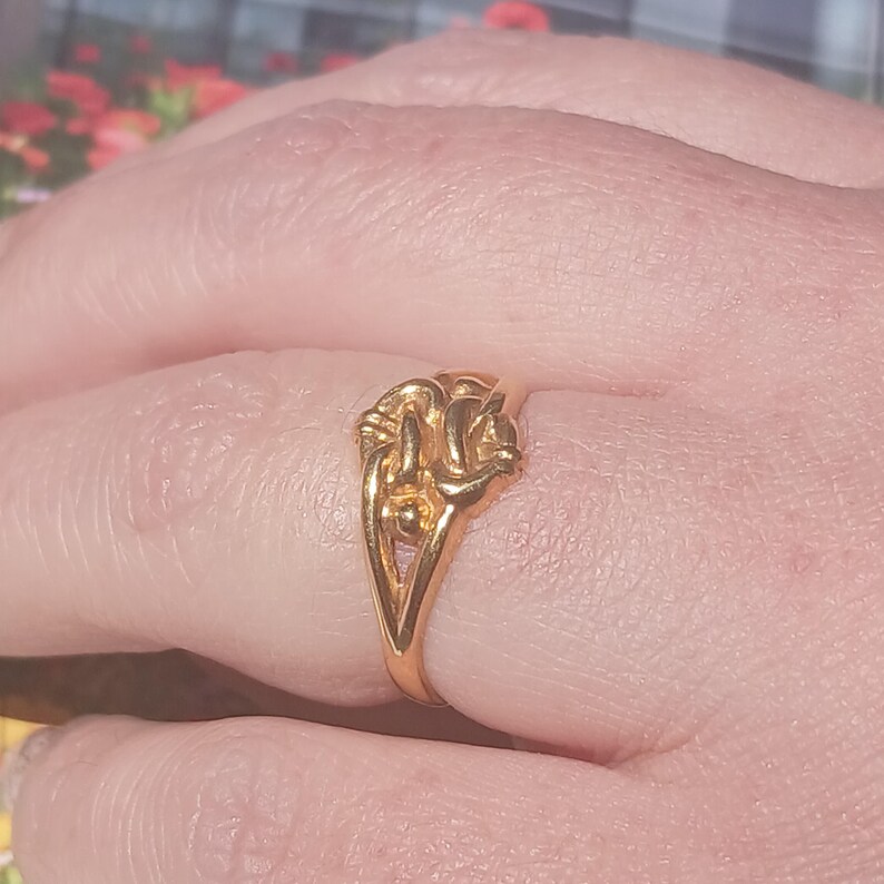 May include: A gold ring with a knot design. The ring is worn on a finger.