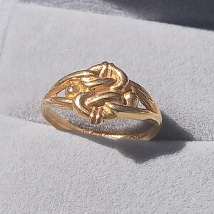 May include: A gold ring with a knot design. The ring is made of 18 karat gold.