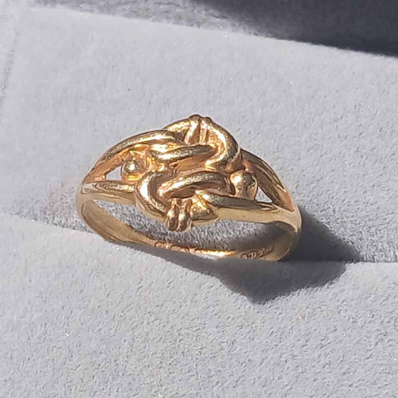 May include: A gold ring with a knot design. The ring is made of 18 karat gold.