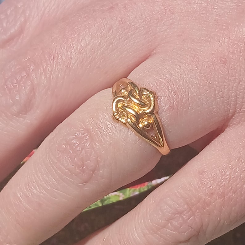 May include: A gold ring with a knot design. The ring is worn on a finger.
