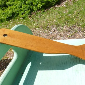 May include: A wooden footrest with a rounded shape and two holes. The footrest is light brown and has a smooth surface.