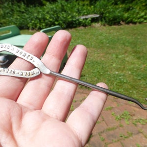 May include: A silver shoe horn with a hook on one end and a loop on the other. The loop has the text "WELK-OVER SHOES FOR MEN & WOMEN." engraved on it.