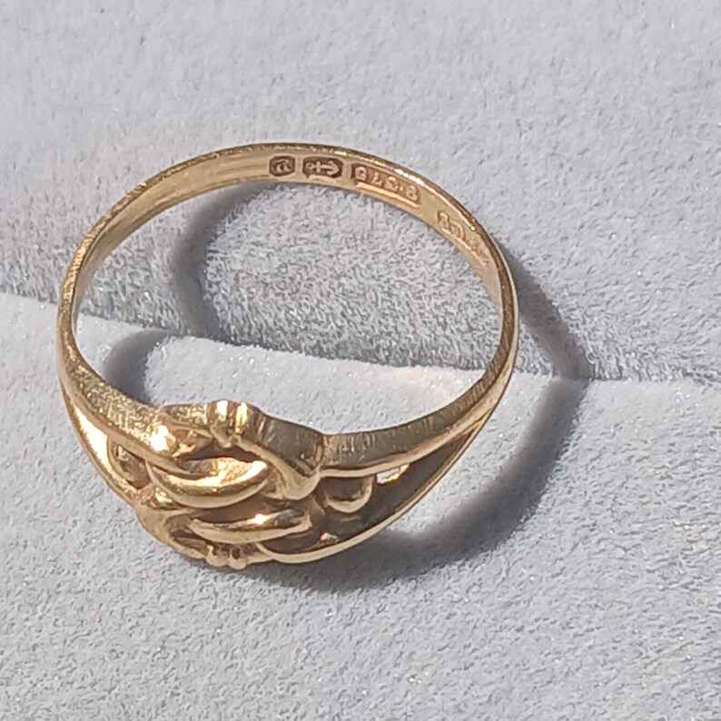 May include: A gold ring with an intricate design. The inside of the band is stamped with "9ct 375" and a maker's mark.