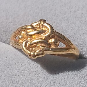 May include: A gold ring with a unique, intricate design featuring multiple interwoven loops and small round accents.