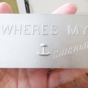 May include: A white metal sign with the text "WHERE'S MY CHICAGO" in raised letters. The sign has a small stylized image of a city skyline.