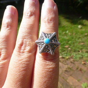 May include: A silver ring with a turquoise stone in the center and a starburst design made of marcasite stones.