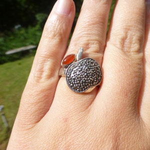 May include: A silver ring with a marcasite apple design and a red gemstone accent.