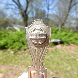 May include: Silver-toned bookmark with a circular design featuring the words "MONTICELLO" and an image of a building. The bookmark has a decorative, ornate design.