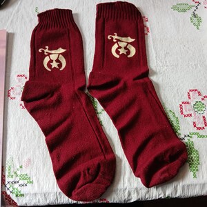 May include: A pair of maroon socks with a white crescent moon and star design. The design also includes a small sword.