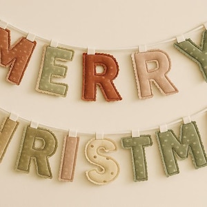 May include: A festive "MERRY CHRISTMAS" banner in various colors, including red, green, and beige. The letters are made of fabric and strung on a white cord, perfect for holiday decor.