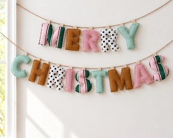 May include: A two-row fabric banner spelling Merry Christmas with stuffed, plush letters. The letters feature various patterns including green and pink stripes, solid brown, red and white stripes, and black polka dots on white fabric.