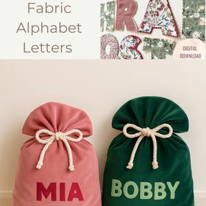 Puede incluir: Sacos de Santa Claus de terciopelo rosa y verde con letras de alfabeto de tela. El saco rosa tiene bordado "MIA", y el saco verde tiene "BOBBY". Las letras miden aproximadamente 10 cm de alto. La imagen también muestra varias letras de alfabeto de tela.