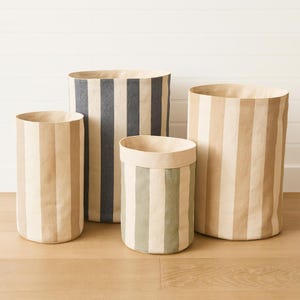 Puede incluir: Cuatro cubos de almacenamiento cilíndricos con rayas verticales en tonos beige, gris y verde. Los cubos tienen diferentes alturas y diámetros, adecuados para organizar objetos en el hogar o la oficina.
