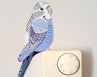 Può includere: Un adesivo di un pappagallo blu e bianco su una parete bianca accanto a un termostato bianco con un quadrante nero e la scritta "MYSON" stampata su di esso.