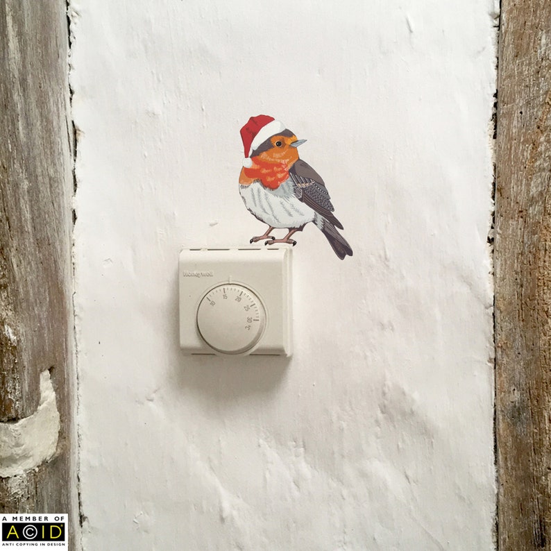 May include: A white thermostat with a round dial and a red-capped robin bird sticker on a white wall.