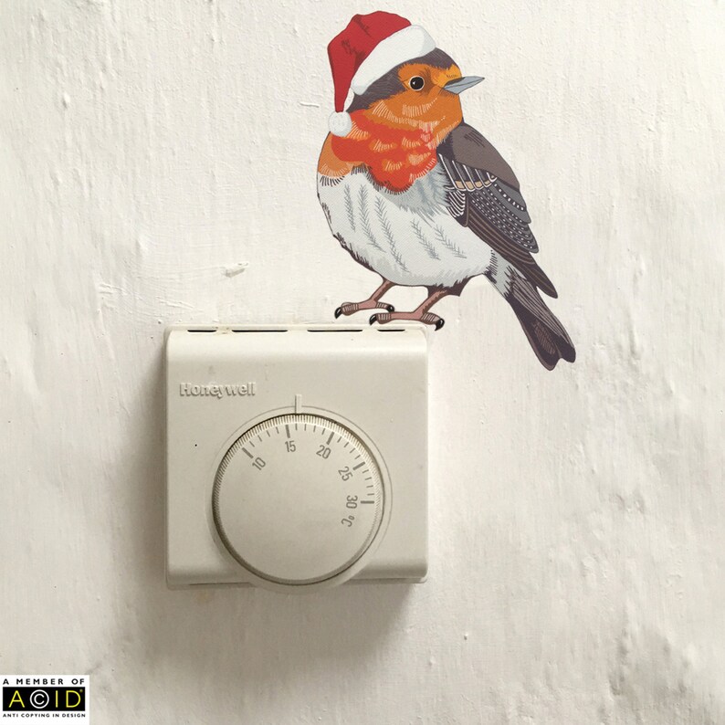 May include: A white Honeywell thermostat with a round dial that goes from 10 to 30 degrees. A red-breasted robin wearing a Santa hat is perched on top of the thermostat.