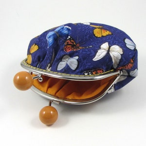 May include: A blue fabric coin purse with a butterfly print and a silver clasp. The purse is open and the inside is lined with orange fabric.