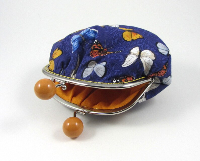 May include: A blue fabric coin purse with a butterfly print and a silver clasp. The purse is open and the inside is lined with orange fabric.