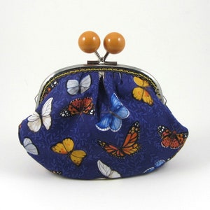 May include: A small blue coin purse with a metal clasp and wooden knobs. The purse is decorated with a pattern of colorful butterflies.