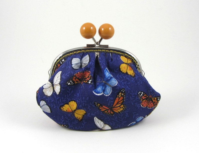 May include: A small blue coin purse with a metal clasp and wooden knobs. The purse is decorated with a pattern of colorful butterflies.