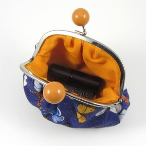 May include: A small, blue fabric coin purse with a butterfly print. The purse is open and has a yellow lining. A small, brown lipstick is inside the purse.