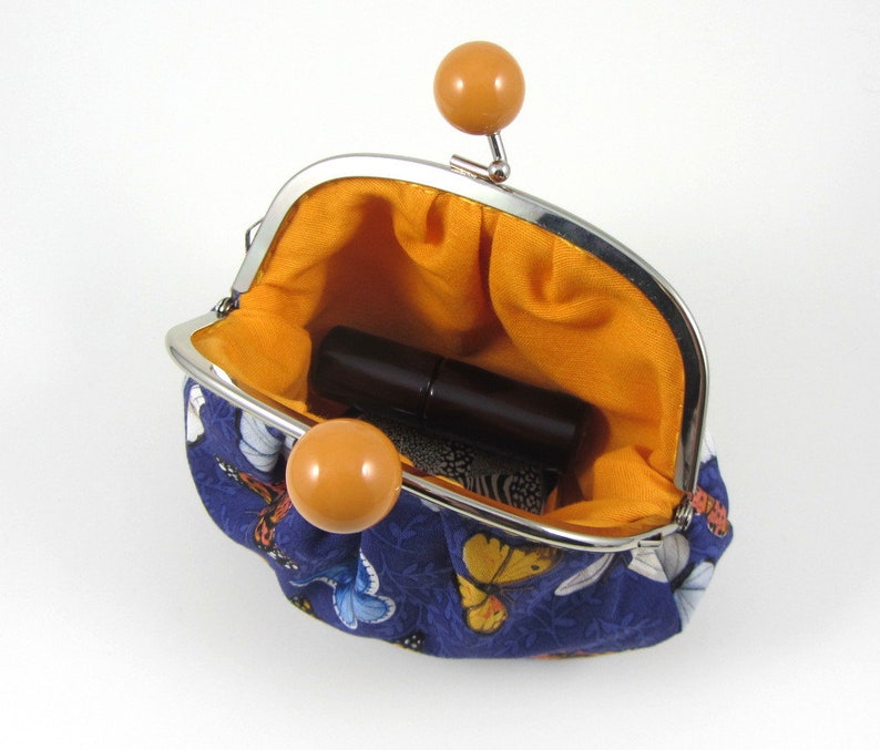 May include: A small, blue fabric coin purse with a butterfly print. The purse is open and has a yellow lining. A small, brown lipstick is inside the purse.