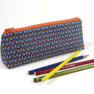 May include: A blue and orange pencil case with a geometric pattern. The case is made of fabric and has a zipper closure. It is lying on a white surface with several colored pencils next to it.