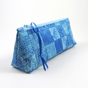 Könnte beinhalten: Ein rechteckiges Etui mit Reißverschluss, das ein Patchwork-Design aus verschiedenen blauen Stoffquadraten aufweist. Der Stoff zeigt diverse Muster, darunter florale und geometrische Motive in hellen und dunklen Blautönen.