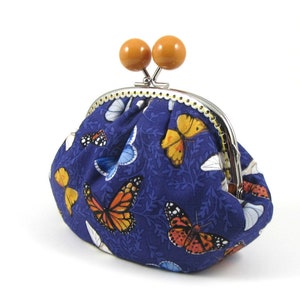 May include: A blue fabric coin purse with a metal clasp and wooden knobs. The purse is decorated with a pattern of butterflies in various colors.