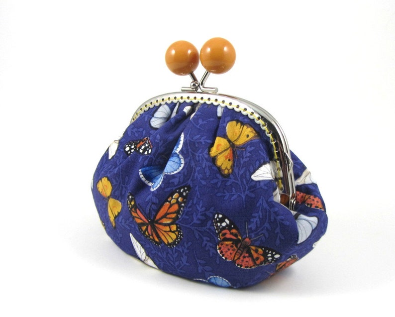 May include: A blue fabric coin purse with a metal clasp and wooden knobs. The purse is decorated with a pattern of butterflies in various colors.