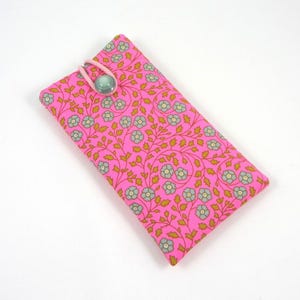 Può includere: Custodia rettangolare in tessuto rosa con un motivo floreale in azzurro e oro. La custodia ha un anello elastico rosa e una chiusura con bottone verde. La custodia è probabilmente per occhiali o un telefono.