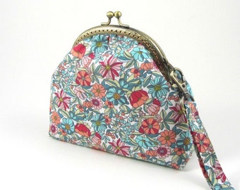 May include: A floral patterned coin purse with a brass clasp and a detachable strap. The purse is white with a variety of pink, red, and blue flowers.