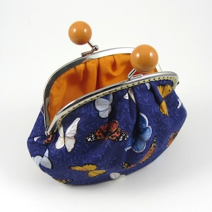 May include: A blue coin purse with a butterfly print and a silver clasp. The purse is open and the inside is lined with orange fabric.